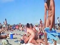 Pareja folla en una playa nudista llena de gente